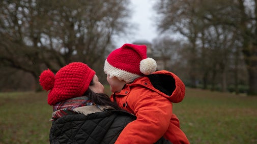 Adult and child dressed in Christmas hats and winter clothes outside in the garden